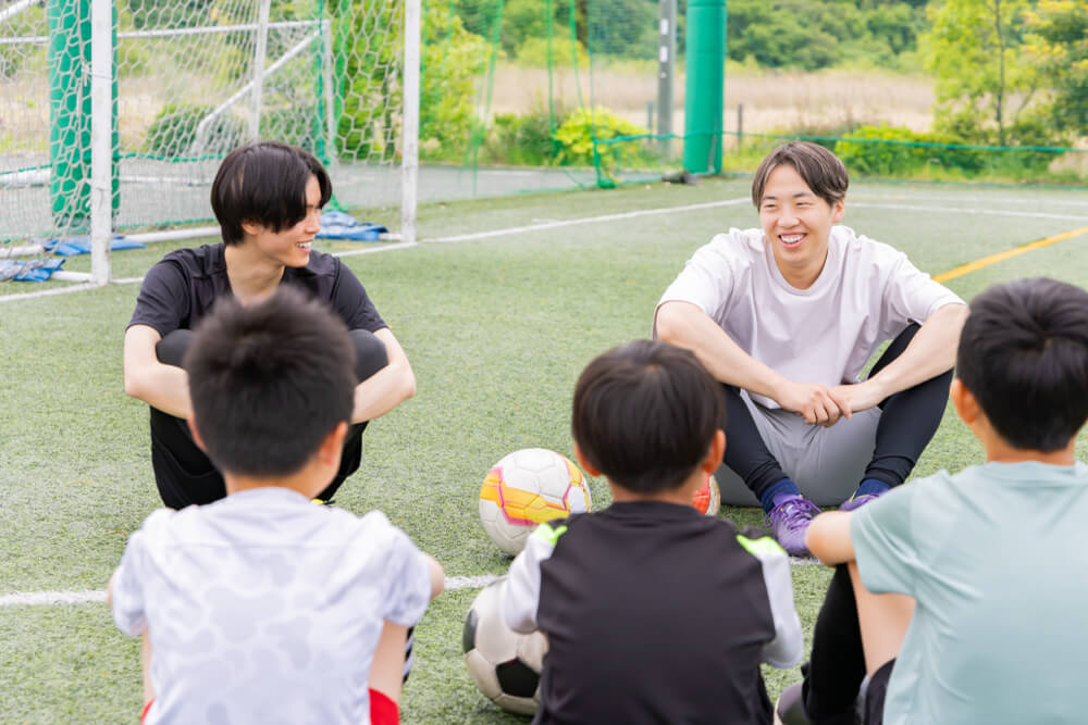 グラウンドで子どもたちと話すサッカーコーチ