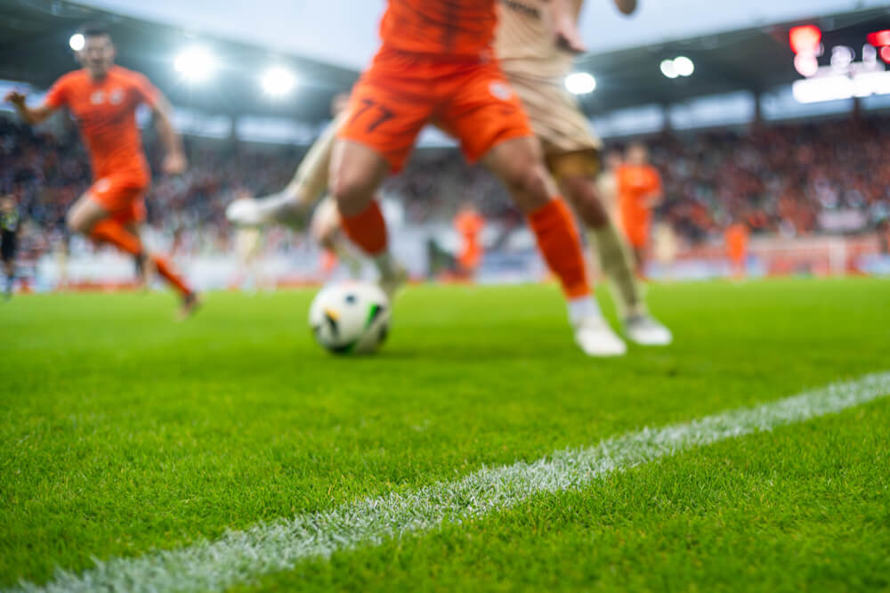 スタジアムのタッチライン際でボールを運ぶサッカー選手